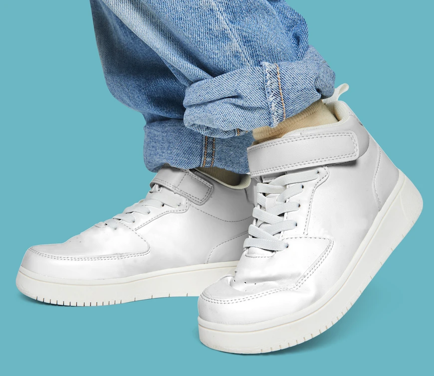 Person wearing light blue jeans and white high-top sneakers with white laces and a velcro strap, standing against a solid light blue background—perfect style inspiration for your next household item cleaning Syracuse session.