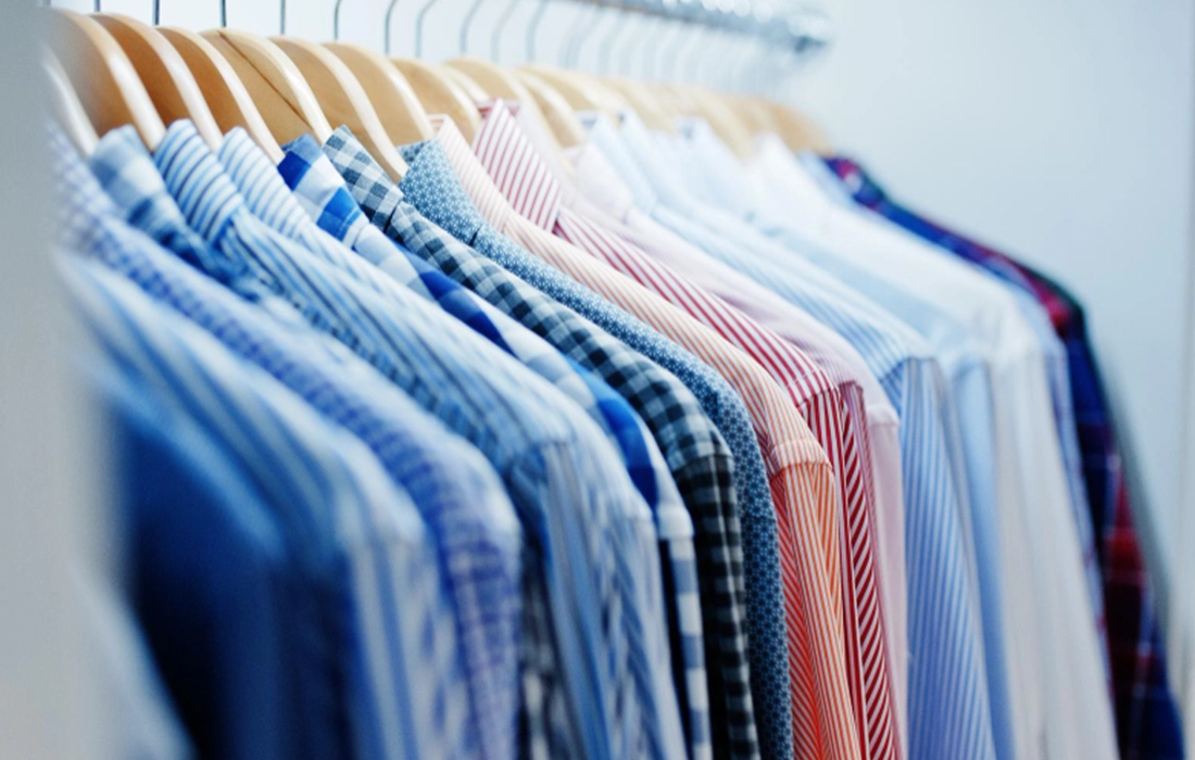 A row of collared shirts in various colors and patterns hanging neatly on wooden hangers in a closet.