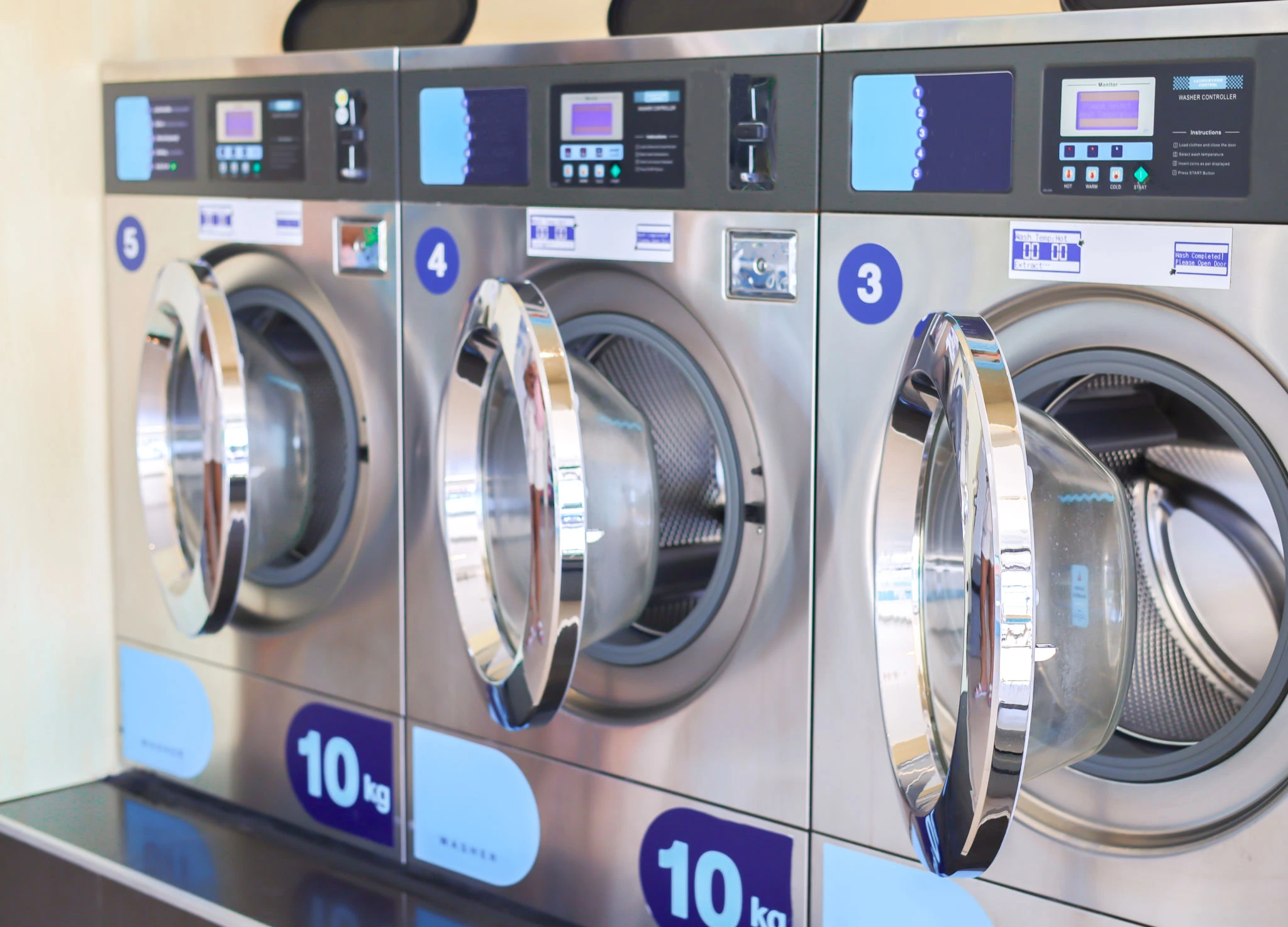 Three industrial front-loading washing machines are lined up side by side, each labeled with a 10 kg capacity and numbered 3, 4, and 5.