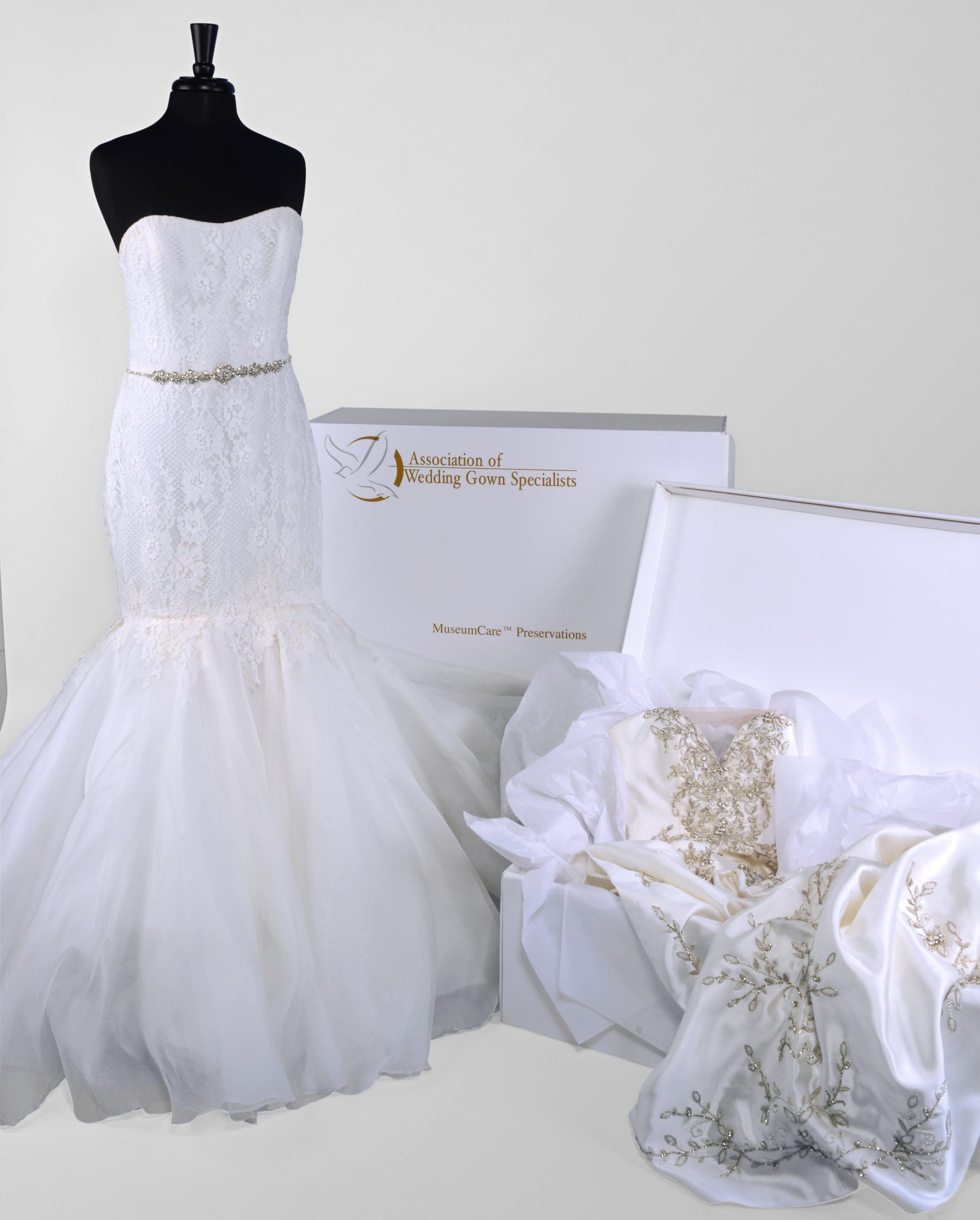 A mermaid-style wedding dress on a mannequin stands next to a preserved gown in a white box labeled 